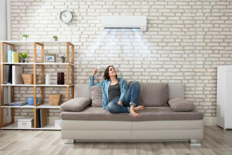 Woman Relaxing on sofa under a wall amounted air conditioning unit